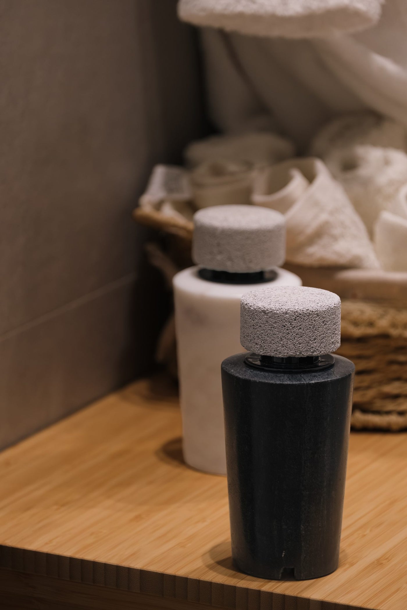 White and dark marble diffusers together on a wooden shelf, rolled towels behind