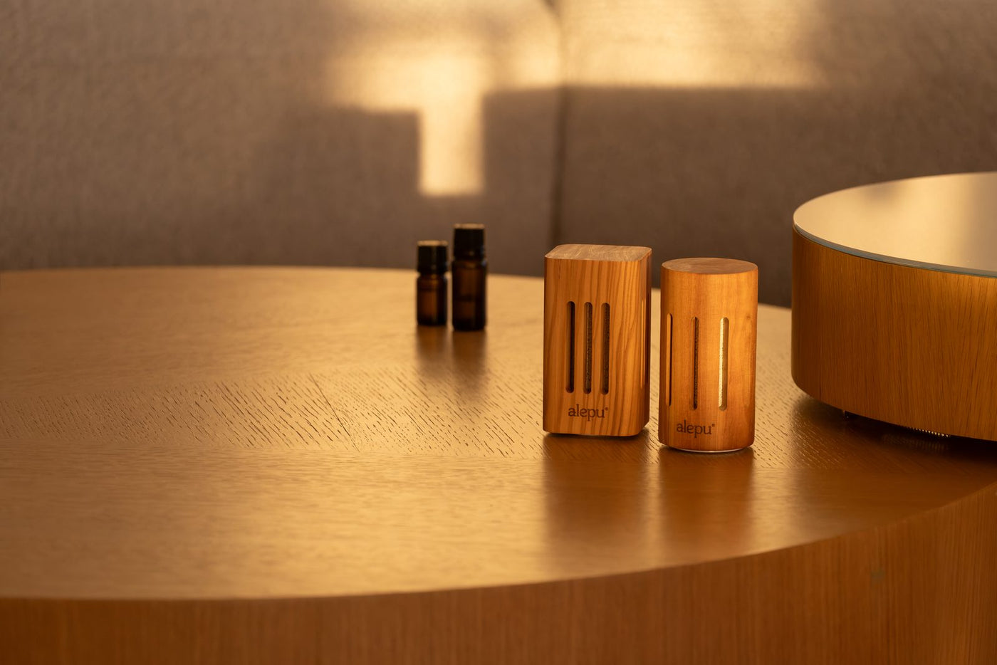 The two olive wood diffusers and two bottles of oil on a wooden table in late sun