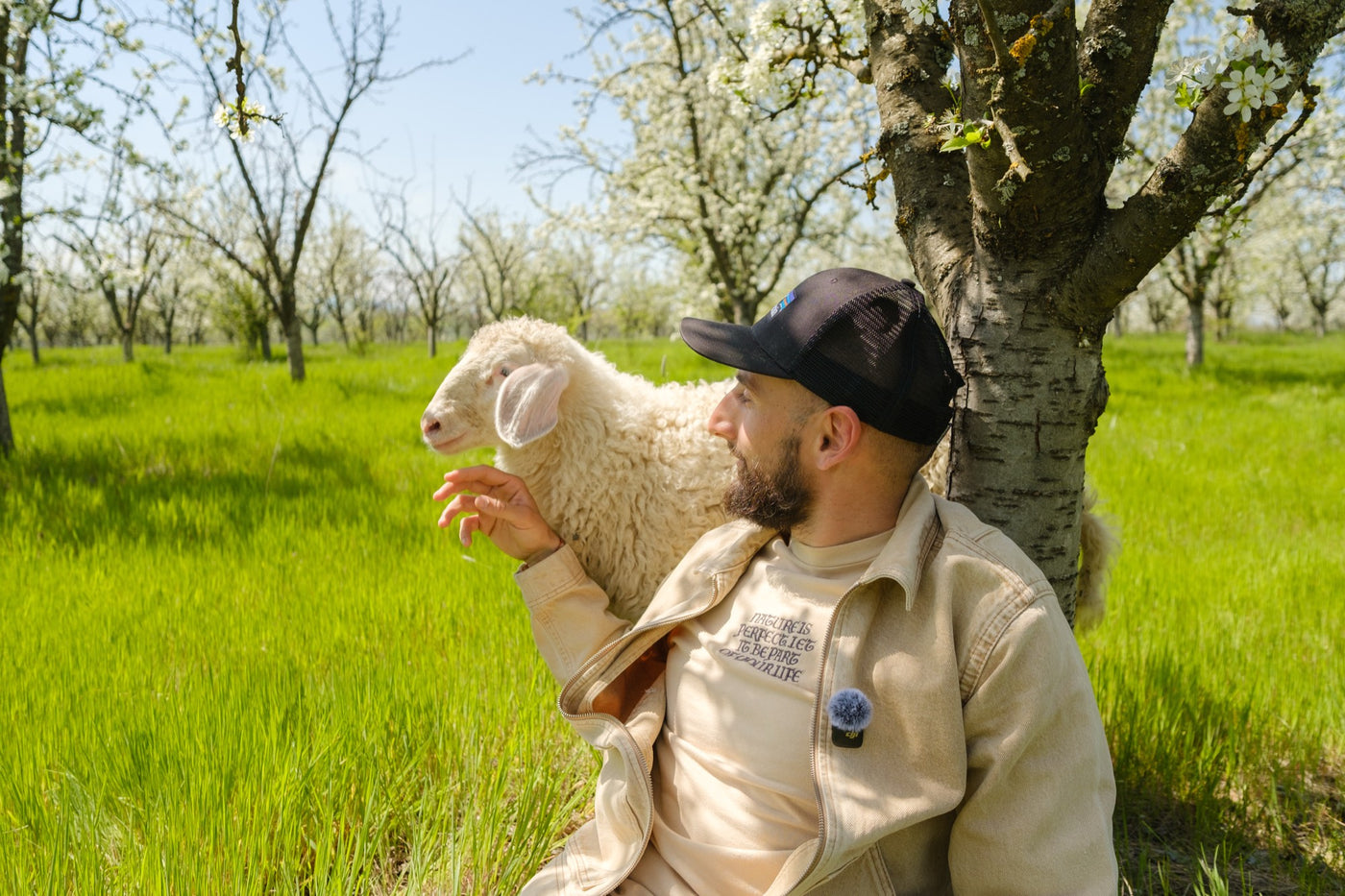 A man in the orchard holding a lamb up on his shoulder