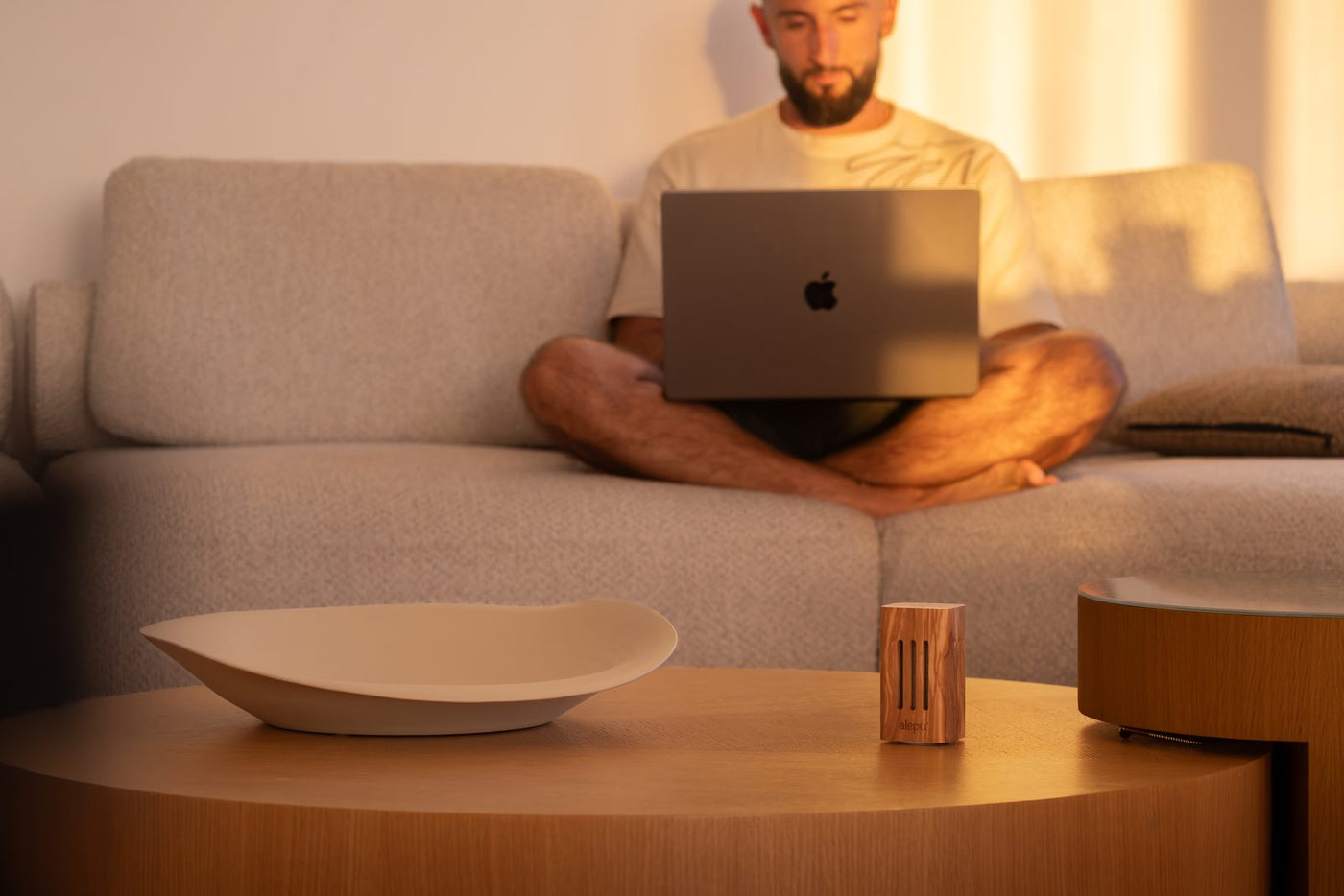 Someone on a sofa at golden hour, the round olive wood diffuser on the table in front