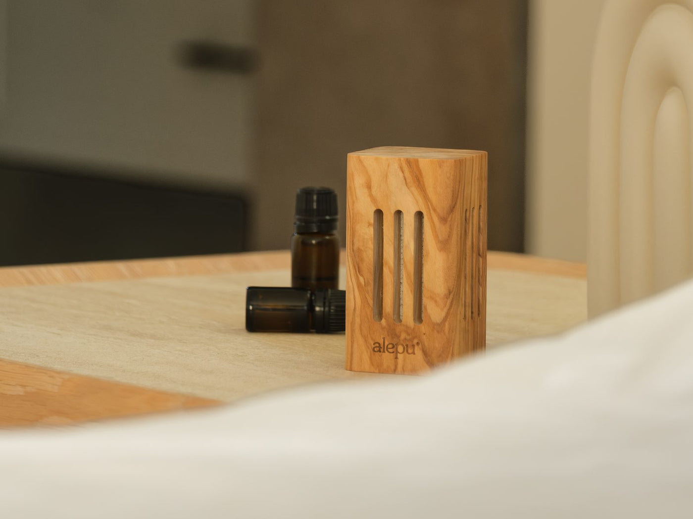 The square olive wood diffuser next to a small bottle of oil on a bedside table