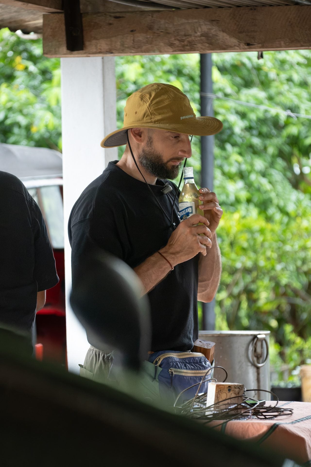 A visitor tasting from a small vessel at a table under an open shelter