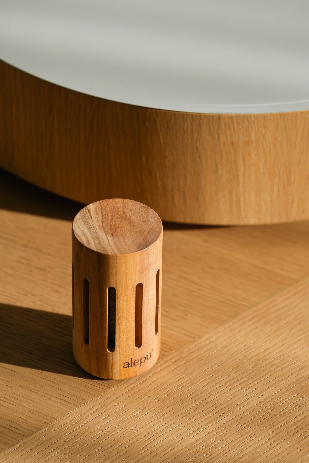 A round olive wood diffuser in low sun on a wooden floor