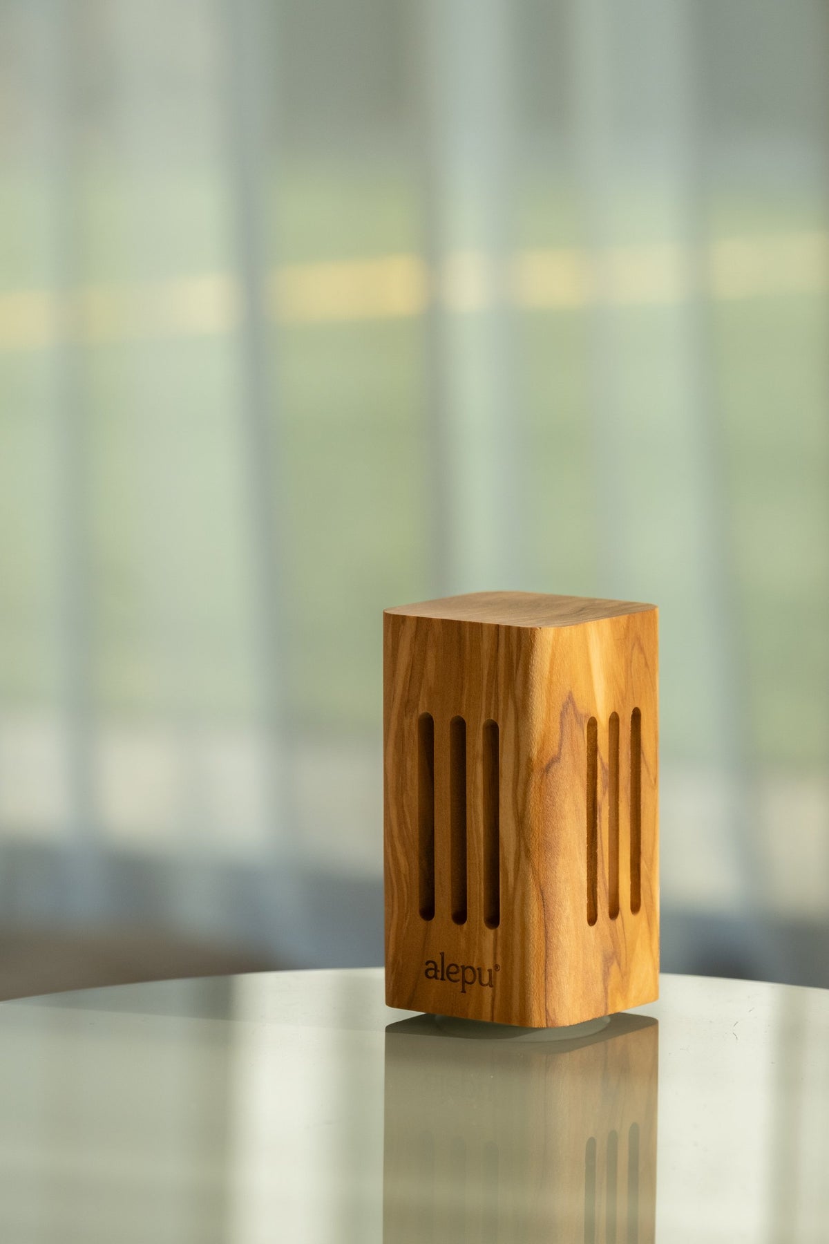 A square olive wood diffuser on a glass table, its slotted sides showing the grain