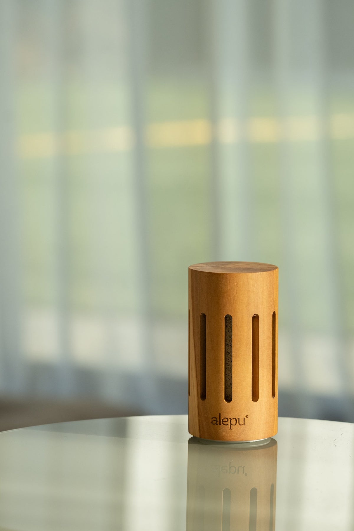 The round olive wood diffuser on a glass table by a window