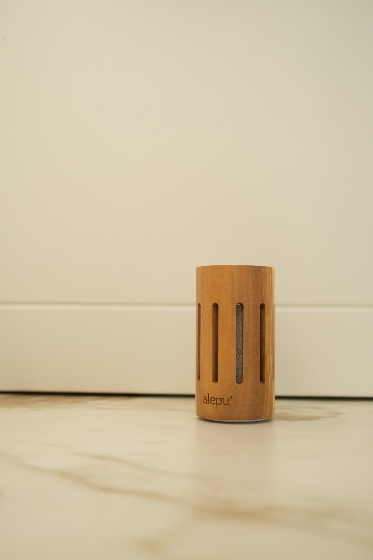 The round olive wood diffuser on a pale marble floor