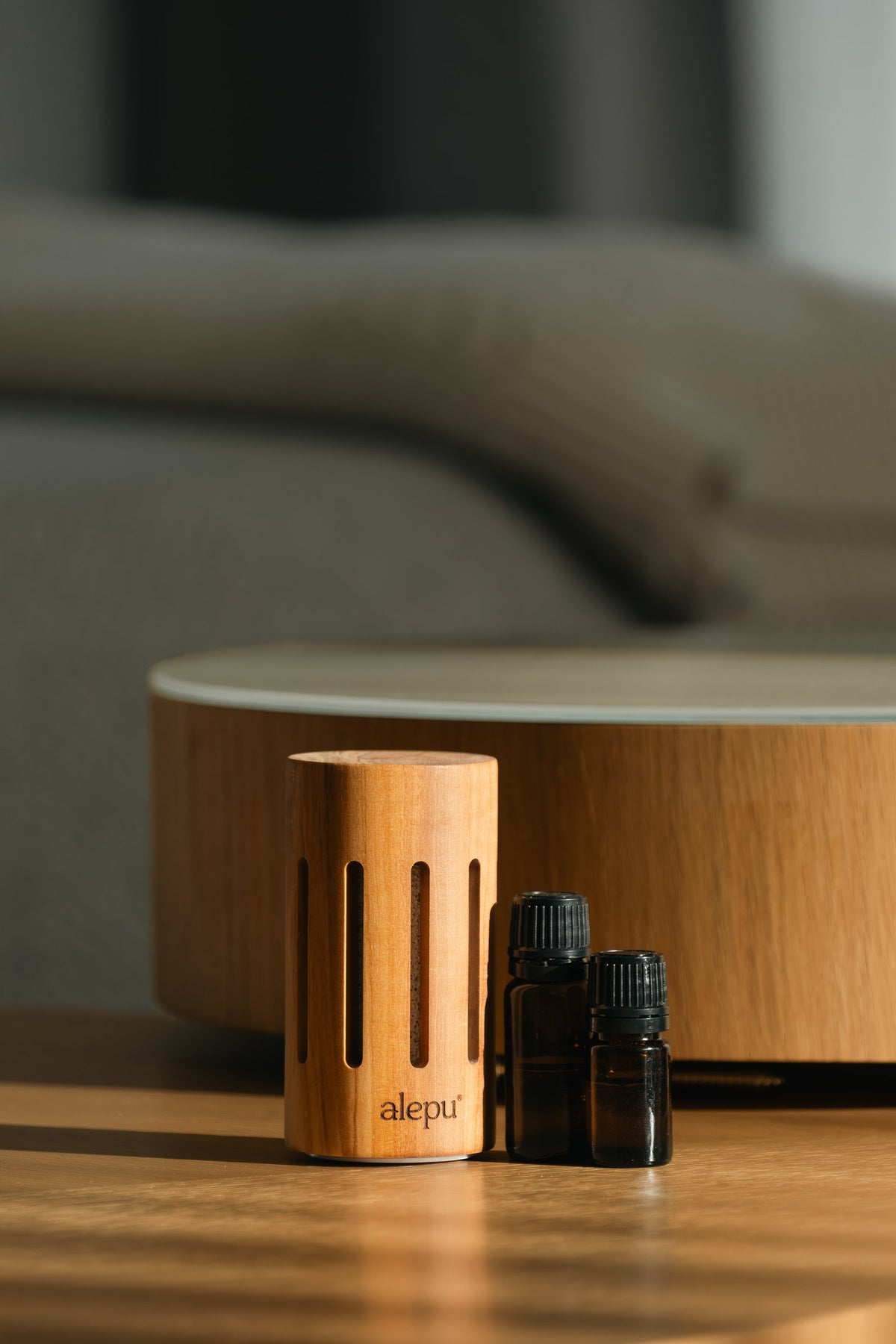 The round olive wood diffuser and two oil bottles in front of a low table
