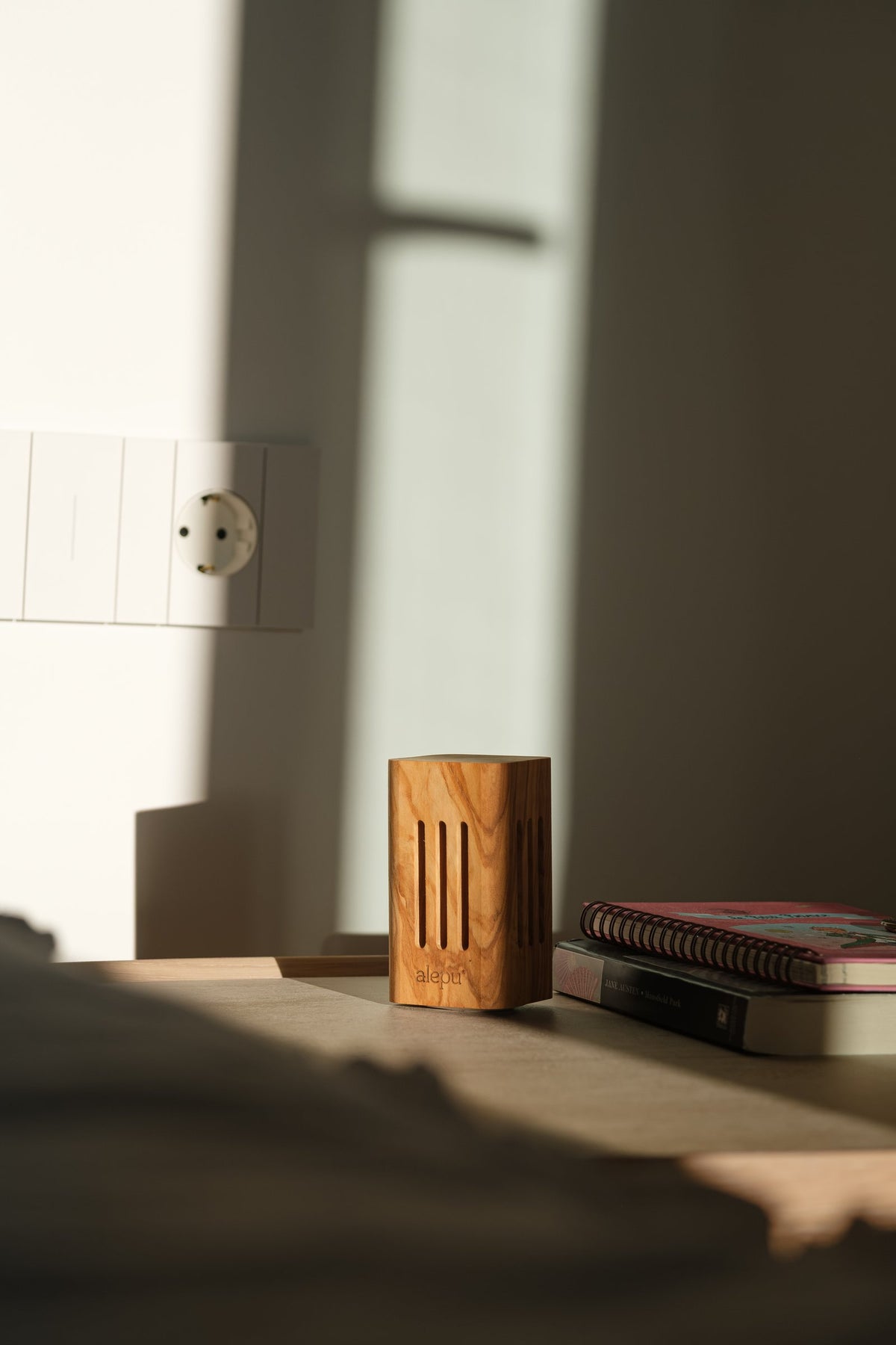 The square olive wood diffuser on a bedside table beside a stack of books