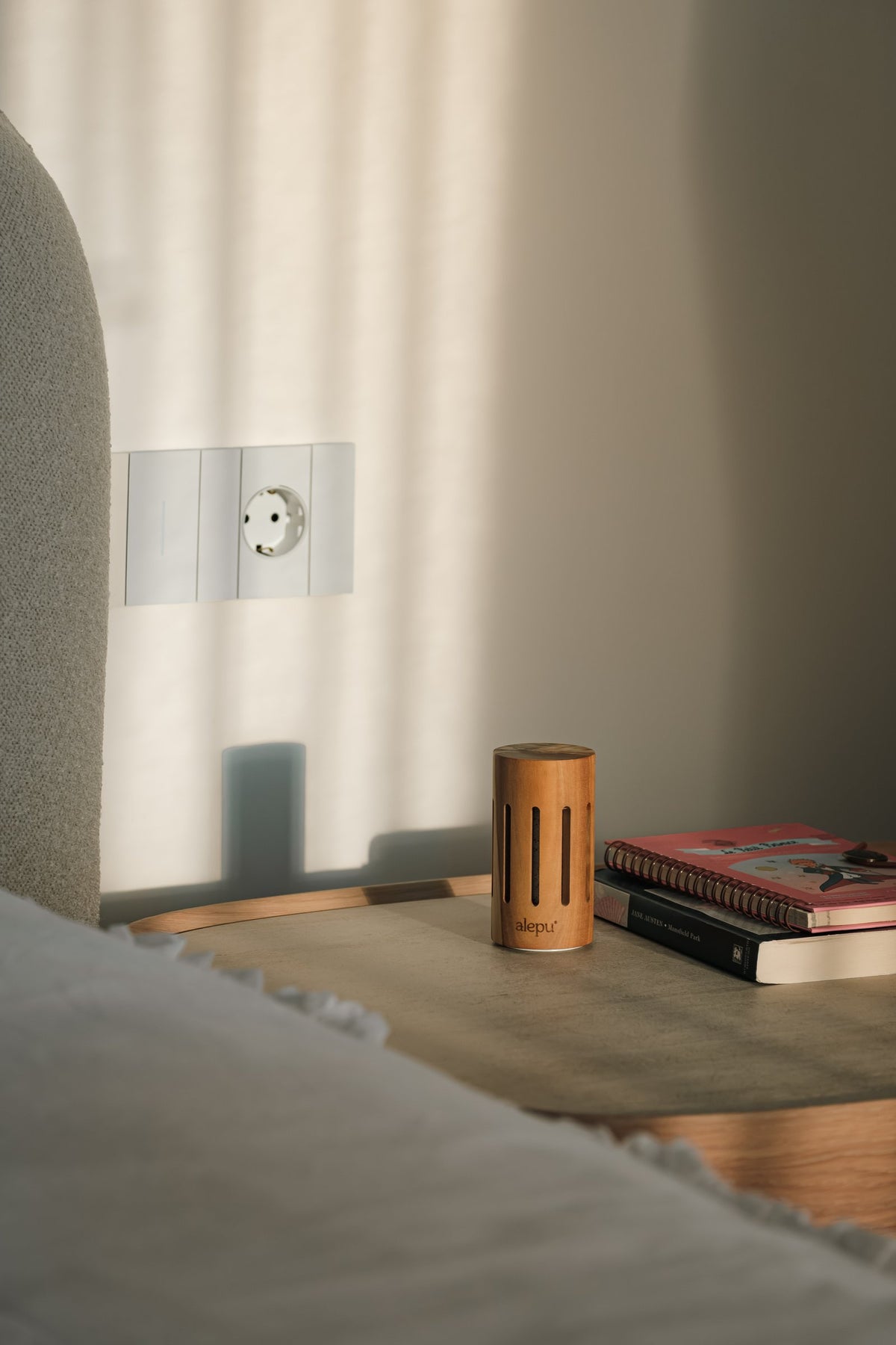 The round olive wood diffuser on a bedside table beside a stack of books