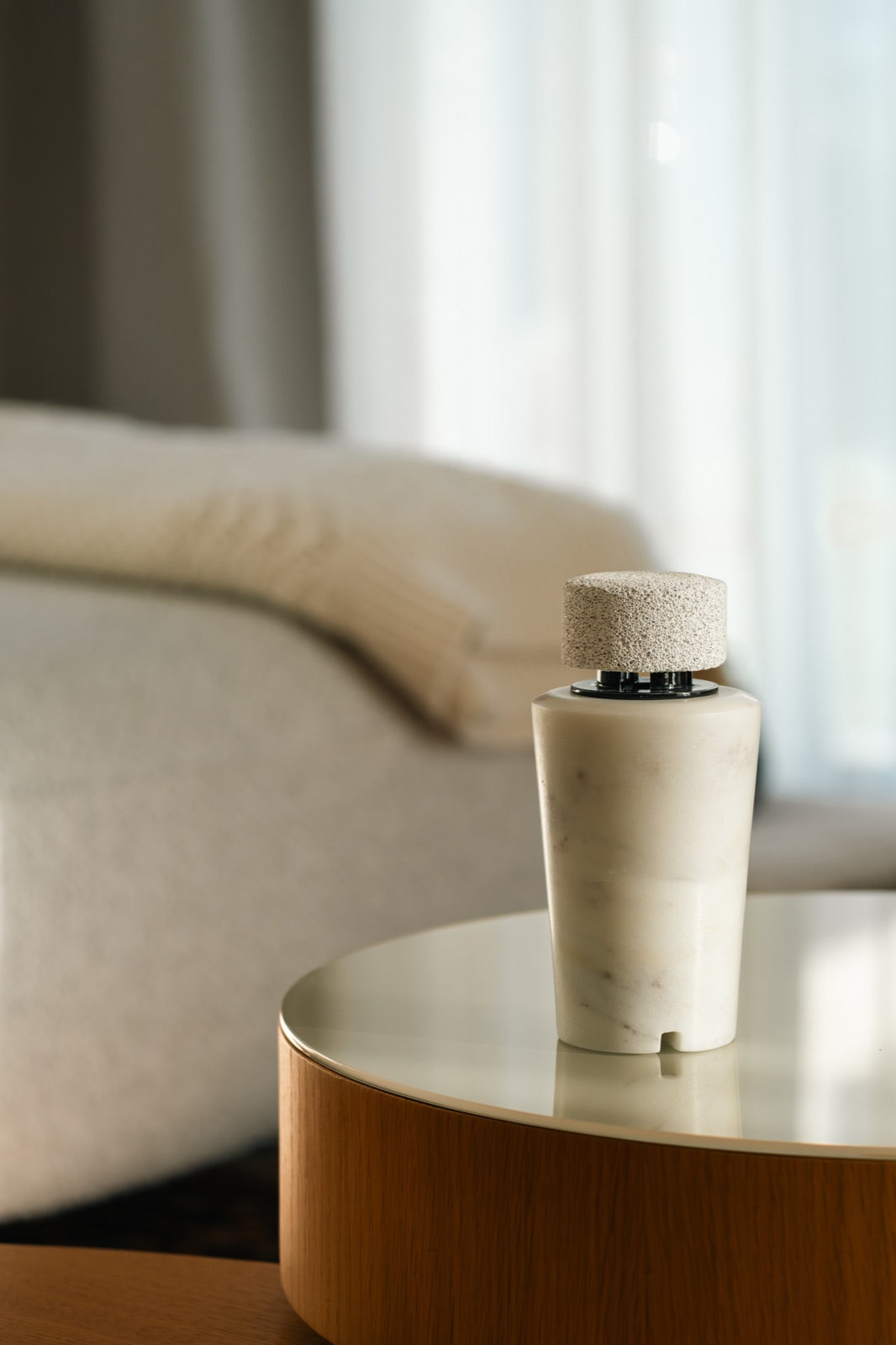 The white marble diffuser on a round wooden side table beside a light grey sofa