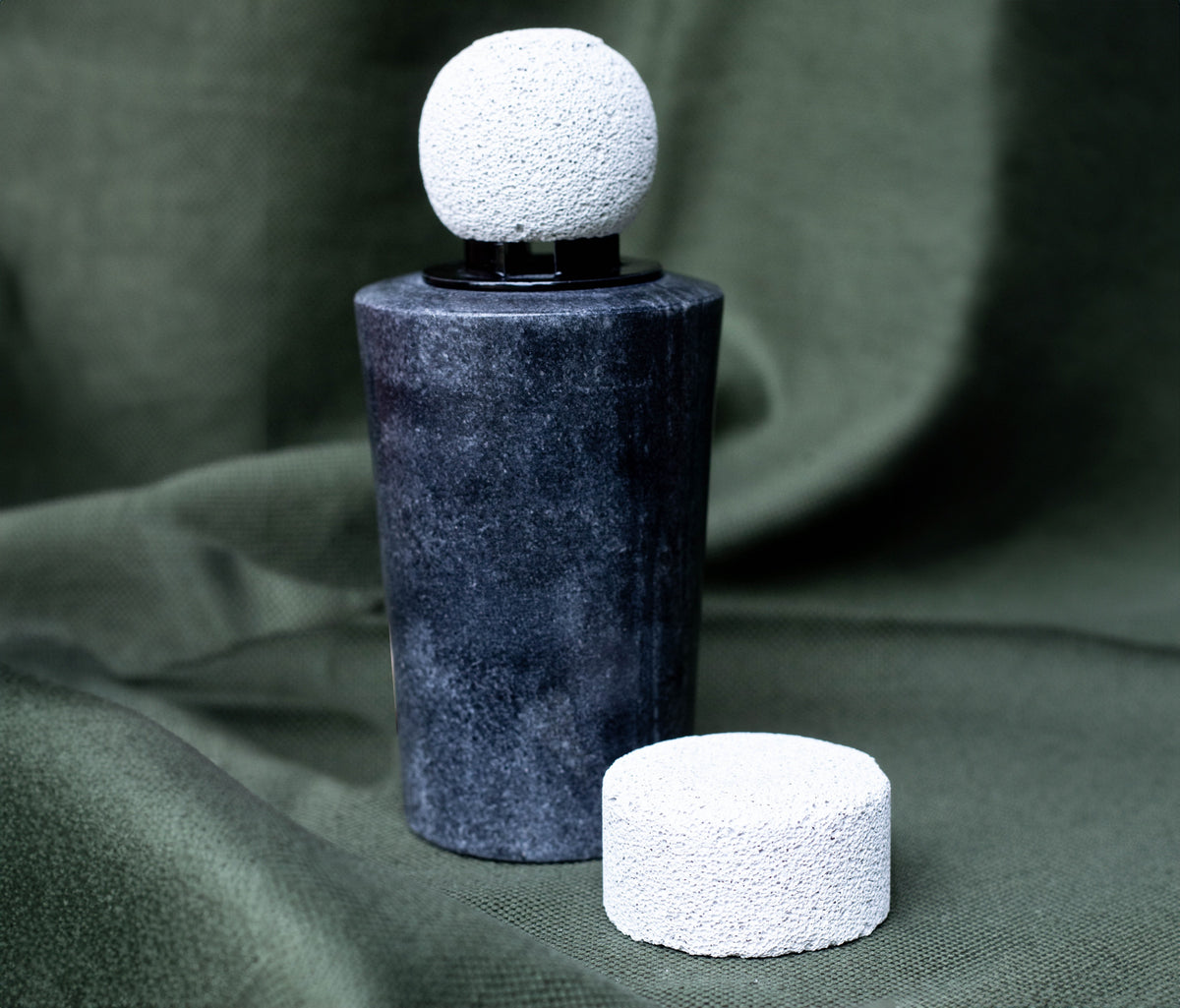 A dark marble Alepu stone diffuser with a white porous ceramic ball, and a second ceramic stone beside it
