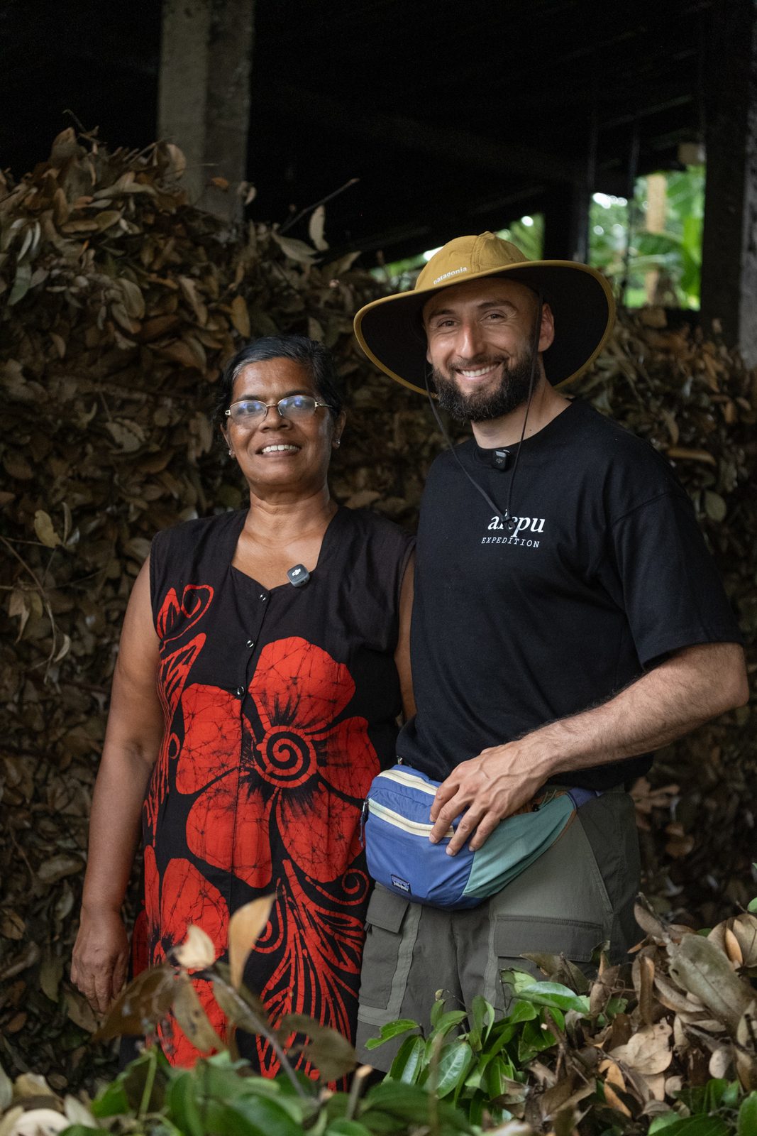 A distiller and Alepu's founder standing together in front of a pile of dried leaves