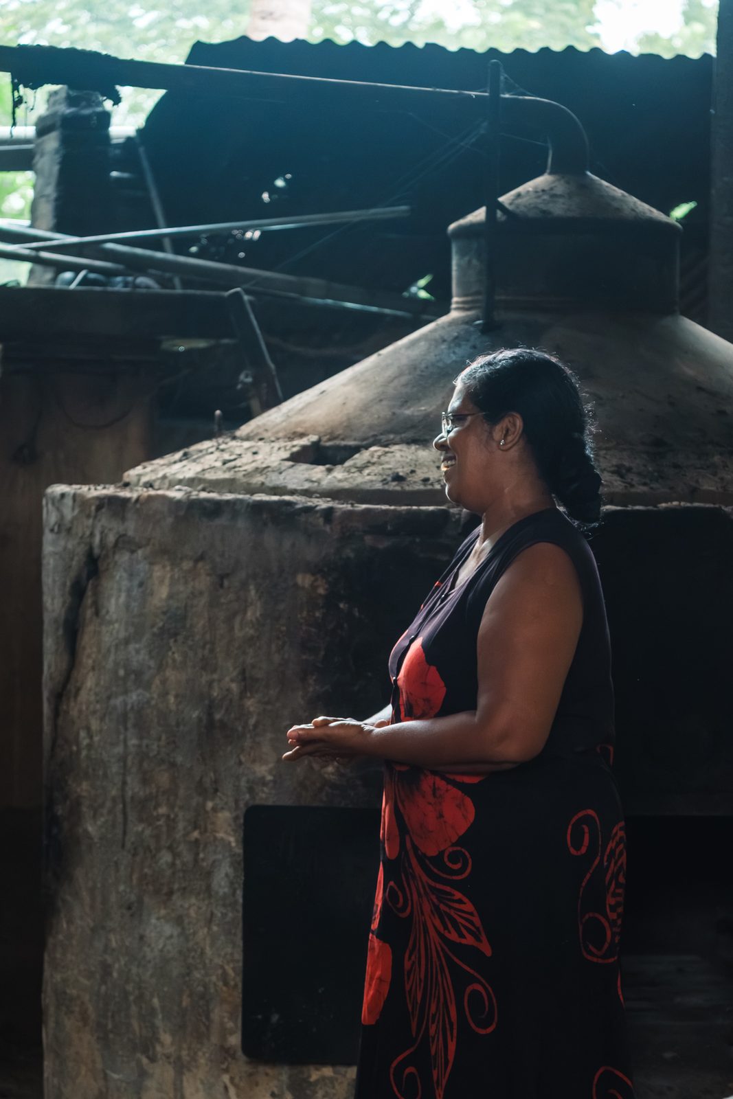 A distiller standing beside a large blackened still in a dim shed