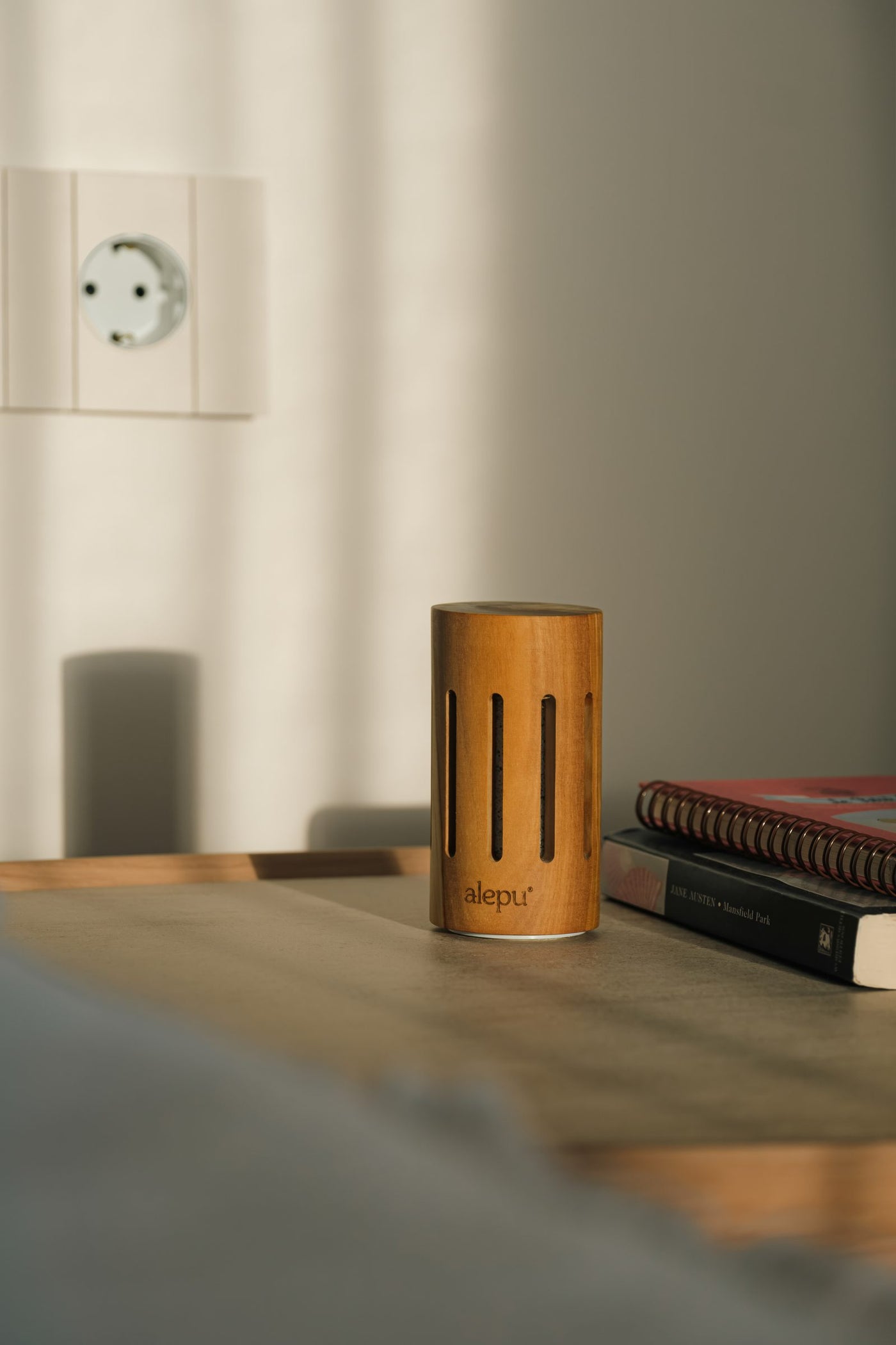 A round olive wood diffuser on a bedside table beside a stack of books