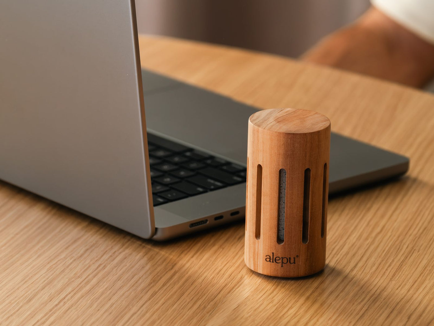 The round olive wood diffuser at the edge of a laptop on a wooden table