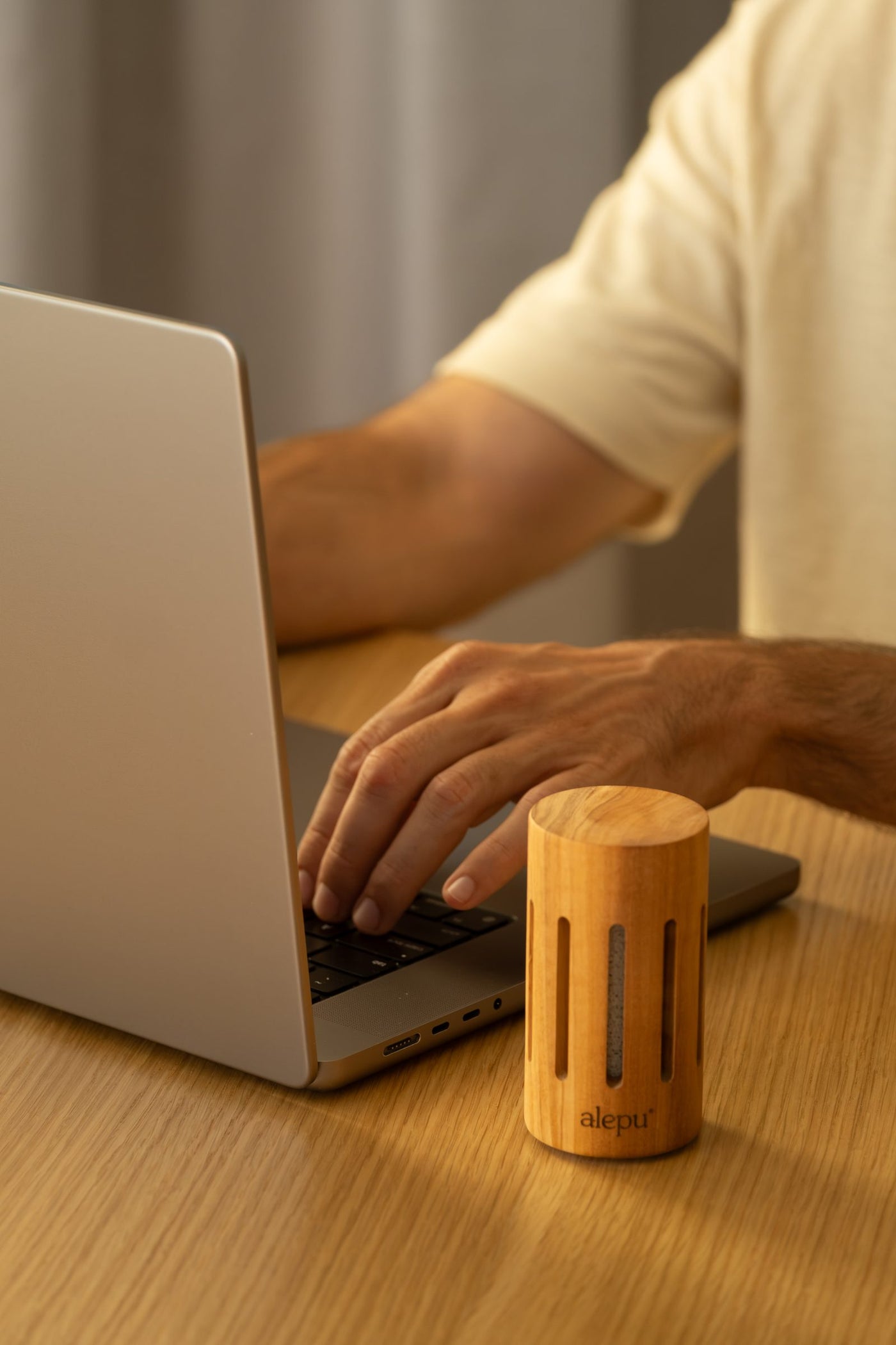 A round olive wood diffuser beside a laptop, a hand on the keyboard