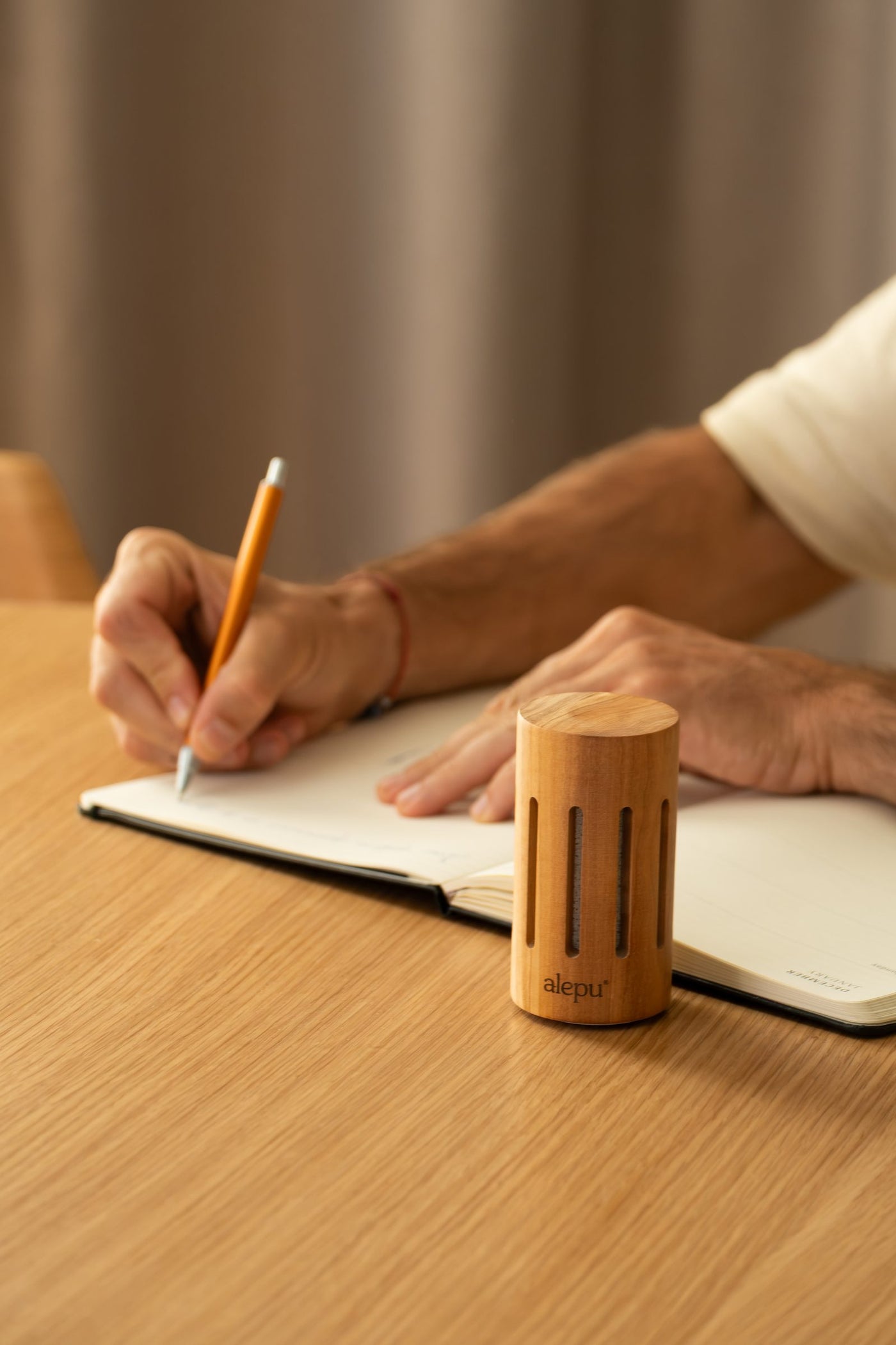 A round olive wood diffuser on a table while someone writes in a notebook