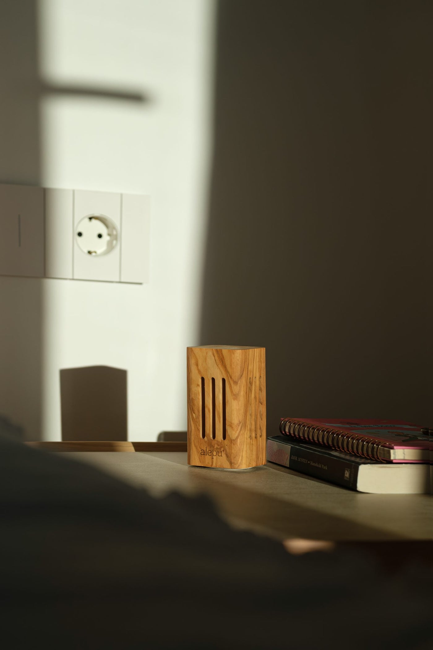 A square olive wood diffuser on a bedside table beside a stack of books