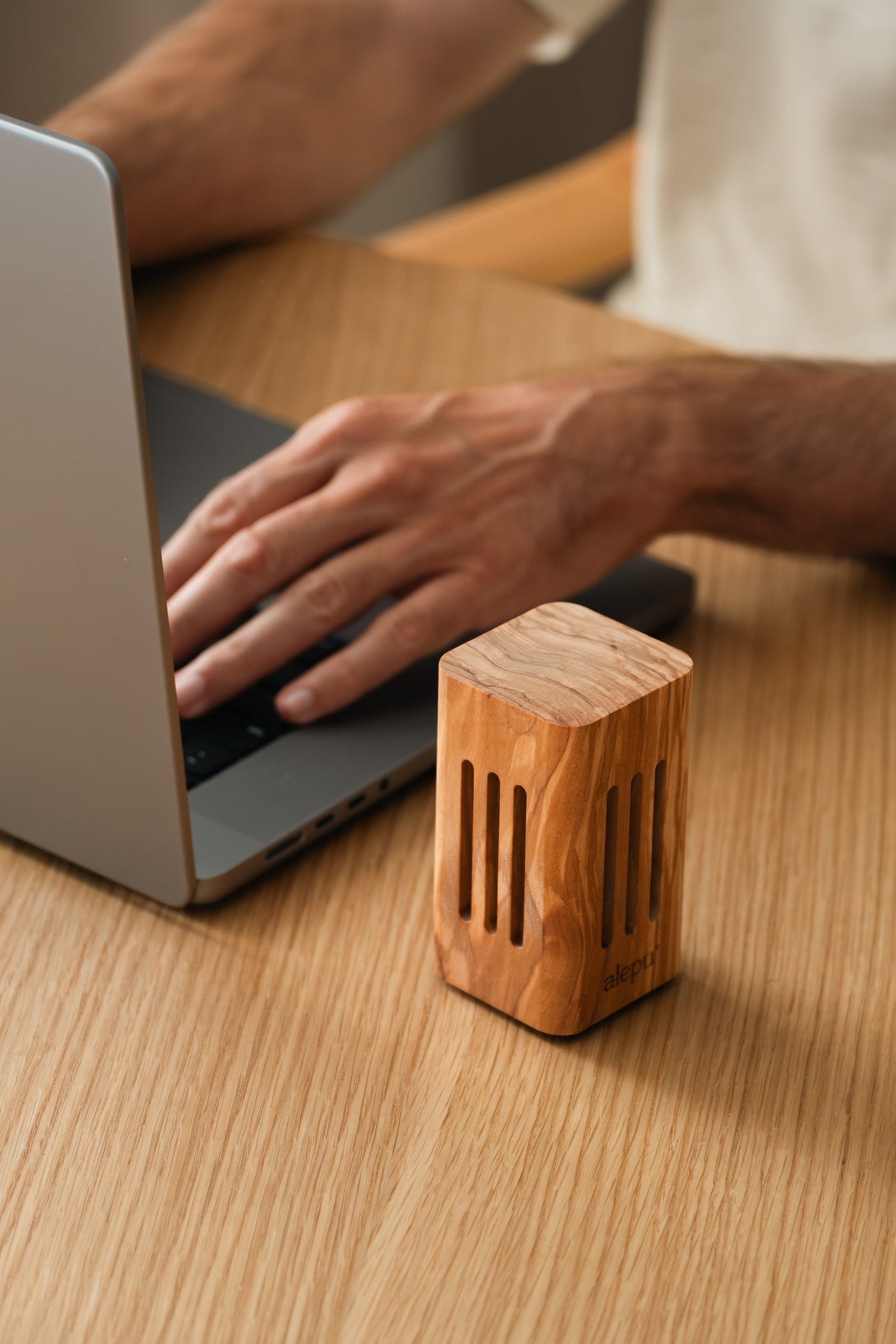 A square olive wood diffuser beside a laptop, a hand on the keyboard