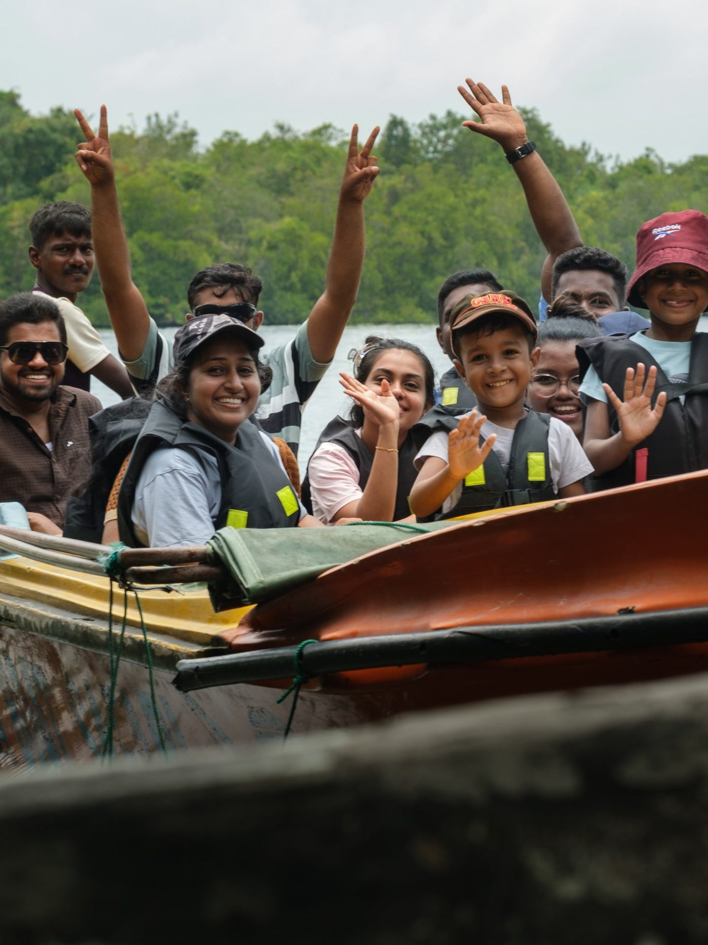 A group in life jackets waving from a boat on a river, forest along the far bank